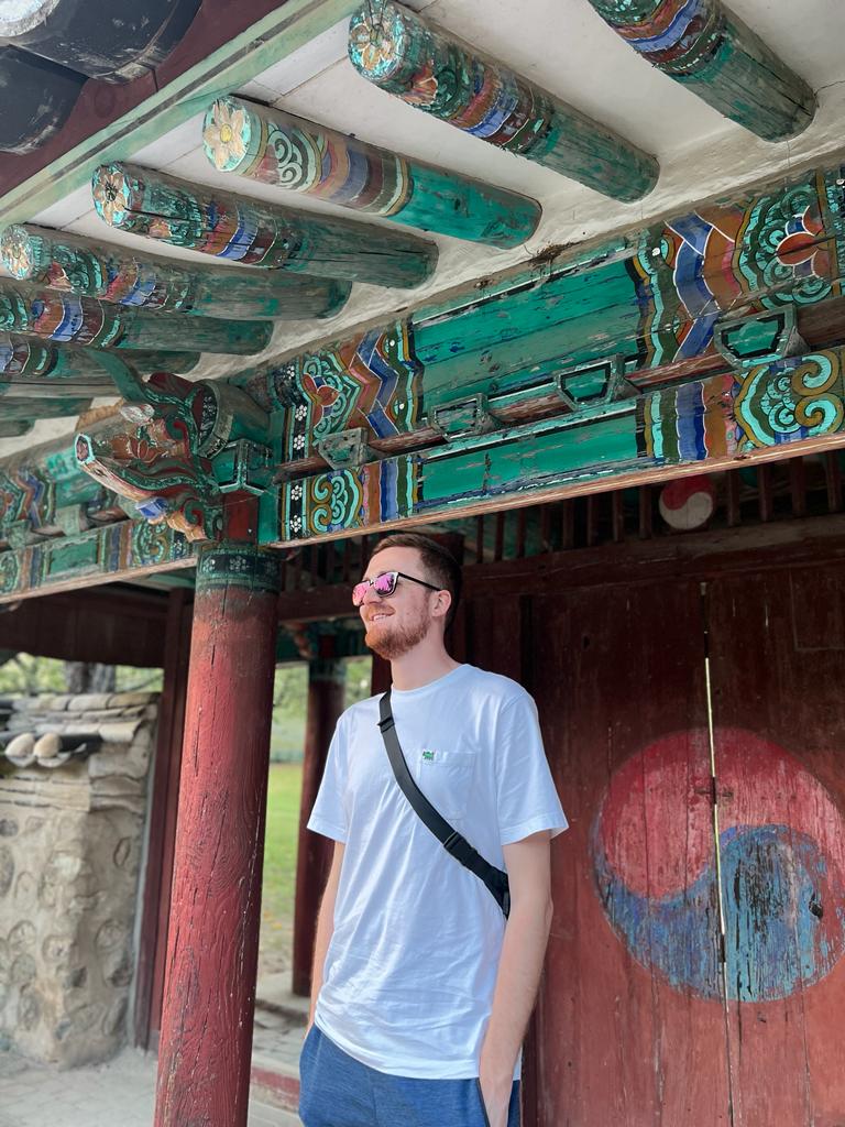 Me, wearing t-shirt and shorts, in front of an old Korean gate in South Korea.